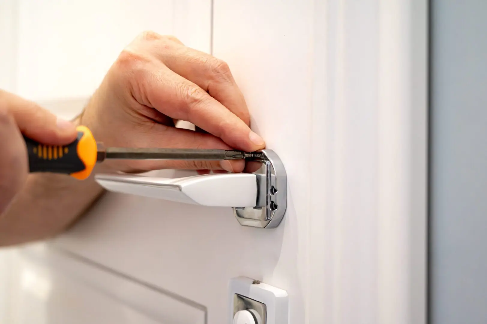 Person fixing a door handle with screwdriver.